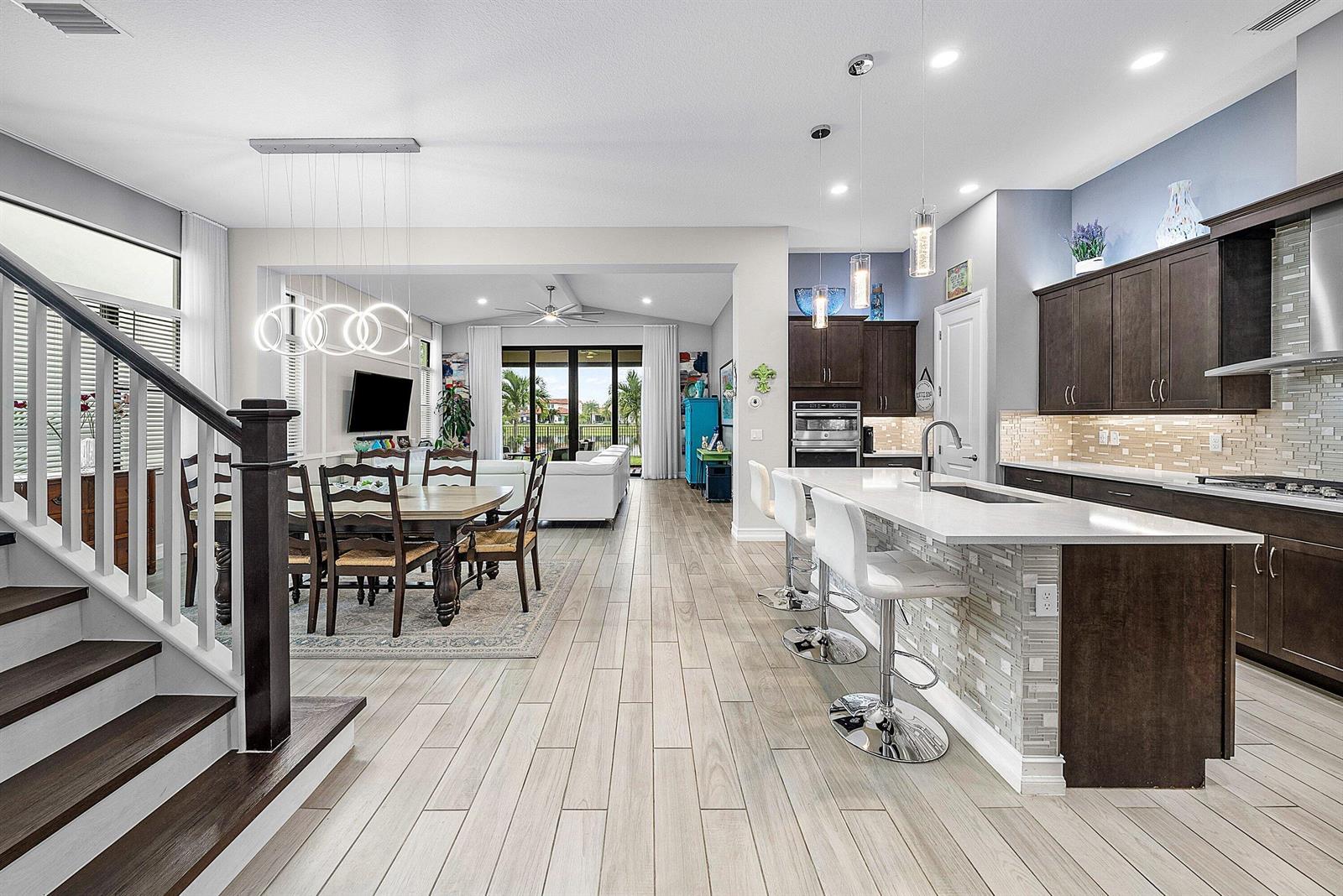 A modern kitchen features dark wood cabinets, a stone-tiled island, and light wood-look flooring — 8884 Grand Prix Lane, Boynton Beach FL 33472, BOYNTON BEACH, FL