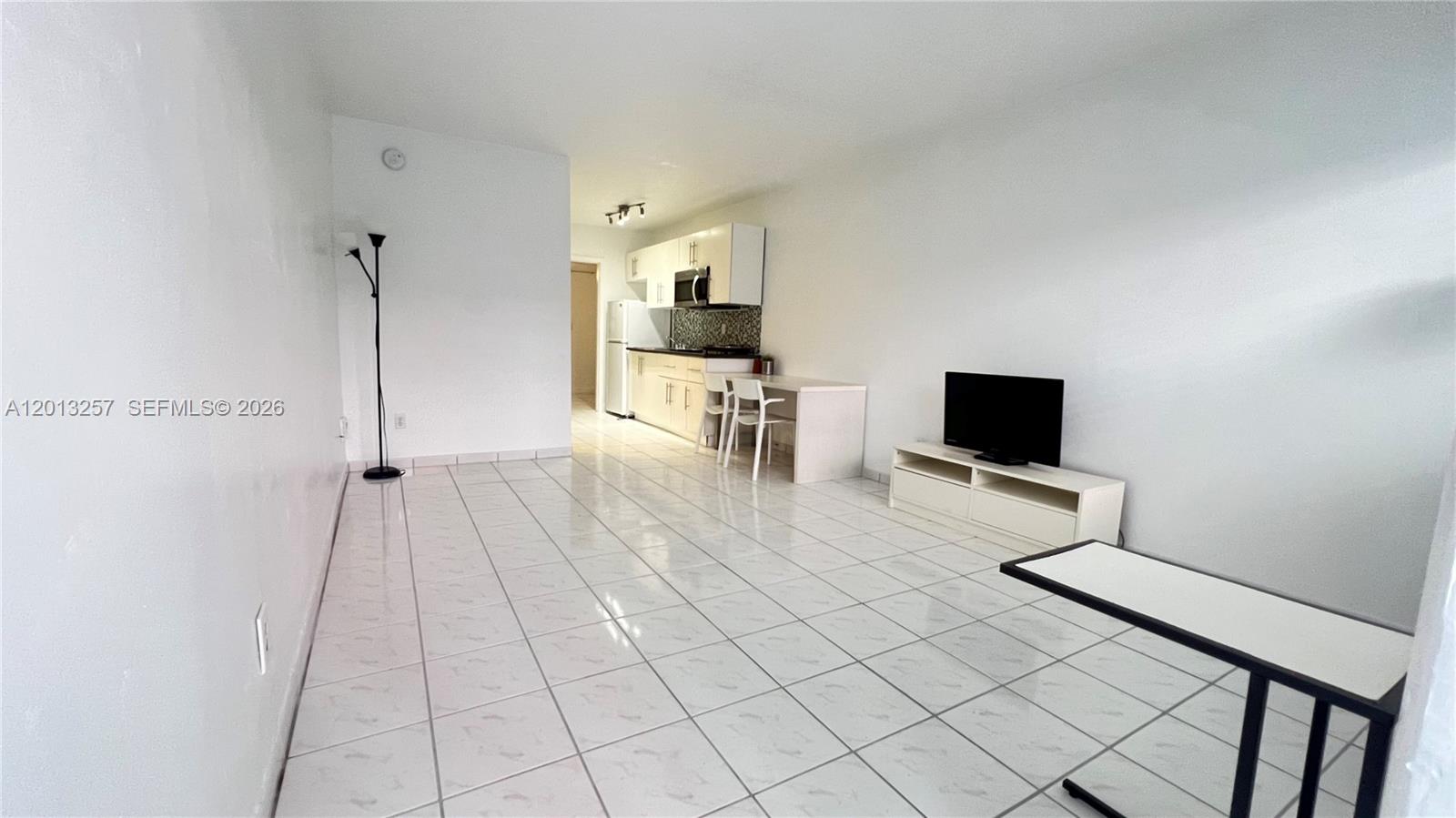 A bright, open-concept living area features white tile flooring, a small kitchen, and a television — 1234 Euclid Ave # 4, Miami Beach FL 33139, MIAMI BEACH, FL