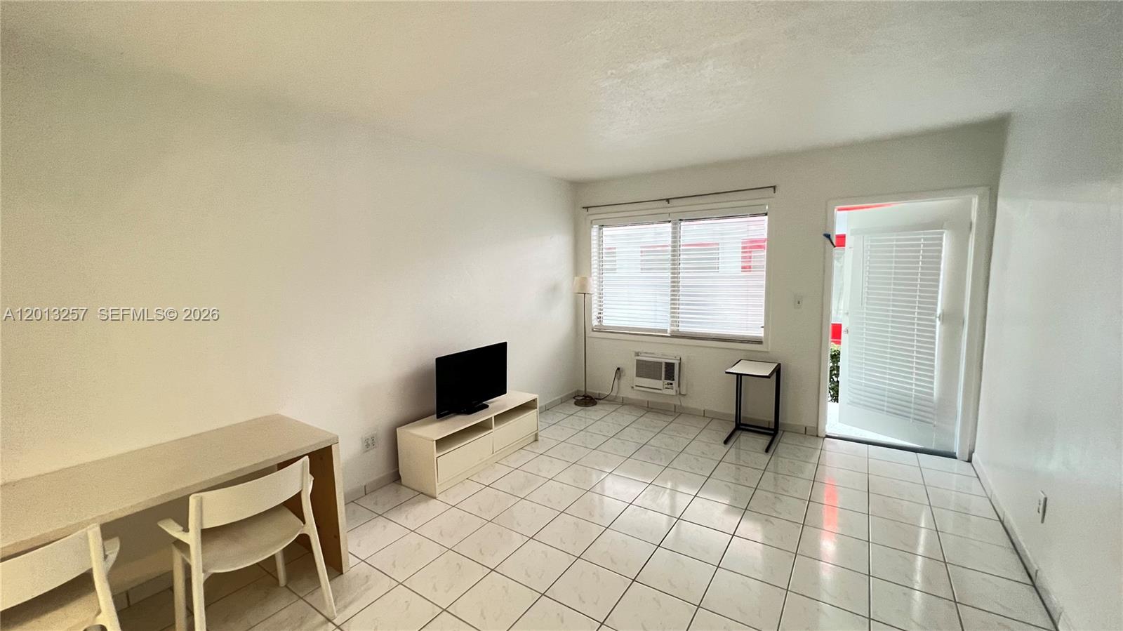 A sparsely furnished room features white walls, tiled flooring, a window, and an open door — 1234 Euclid Ave # 4, Miami Beach FL 33139, MIAMI BEACH, FL