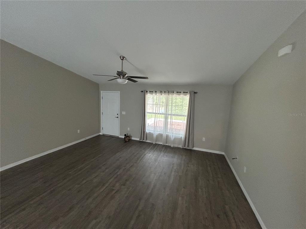 An empty living room features gray walls, dark wood-look flooring, a ceiling fan, and windows — 5092 SW 197TH TERRACE, DUNNELLON, FL