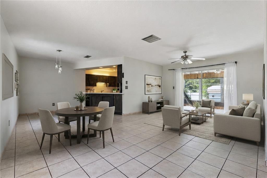 An open-concept living and dining area with tile flooring, neutral furniture, and a kitchen pass-through — 1539 FORT SMITH BOULEVARD, DELTONA, FL