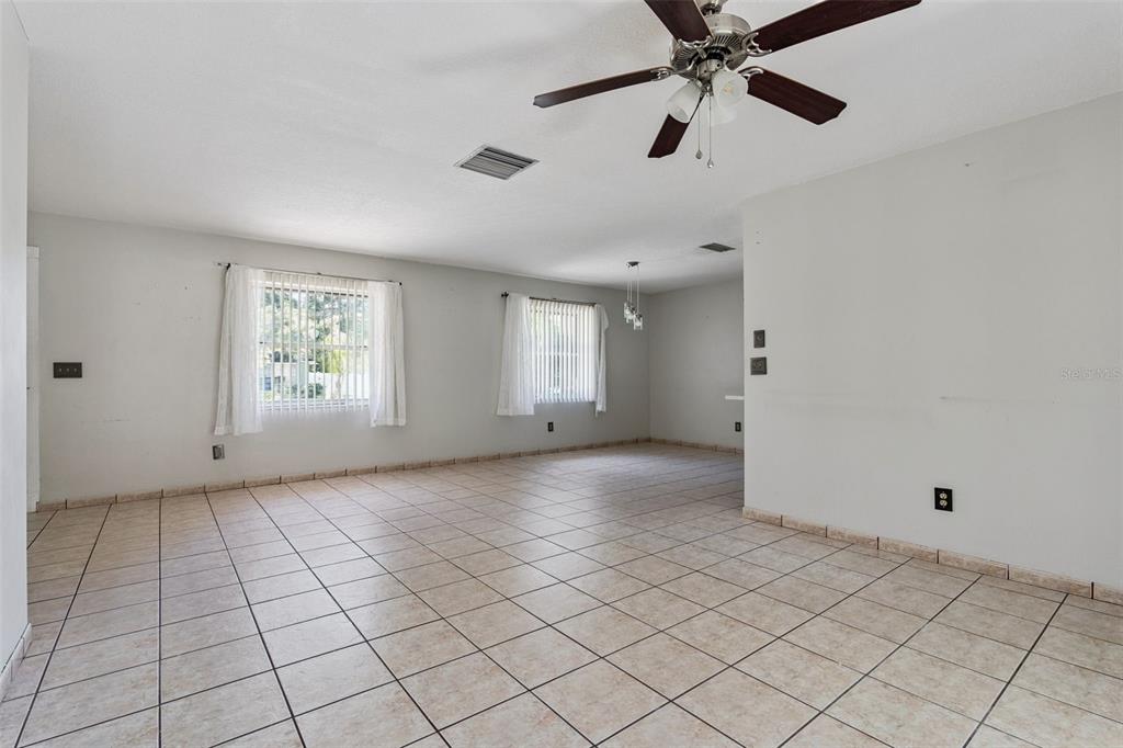 An empty room features light-colored tile flooring, two windows with white curtains, and a ceiling fan — 1539 FORT SMITH BOULEVARD, DELTONA, FL