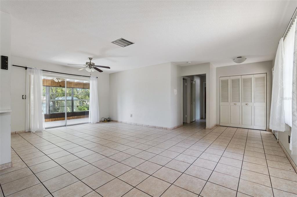 A spacious living room features light-colored tile flooring, white walls, and a sliding glass door — 1539 FORT SMITH BOULEVARD, DELTONA, FL