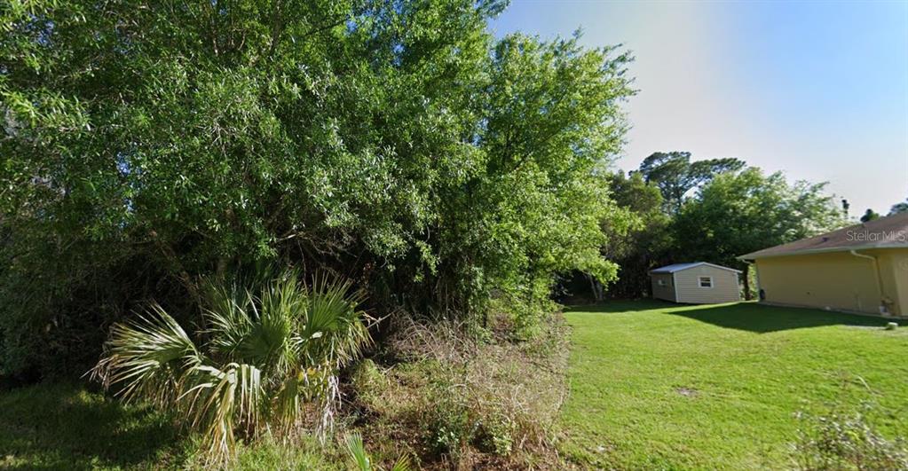 A grassy backyard features a small storage shed and dense trees along the property line — 23509 BRANCH AVENUE, PUNTA GORDA, FL