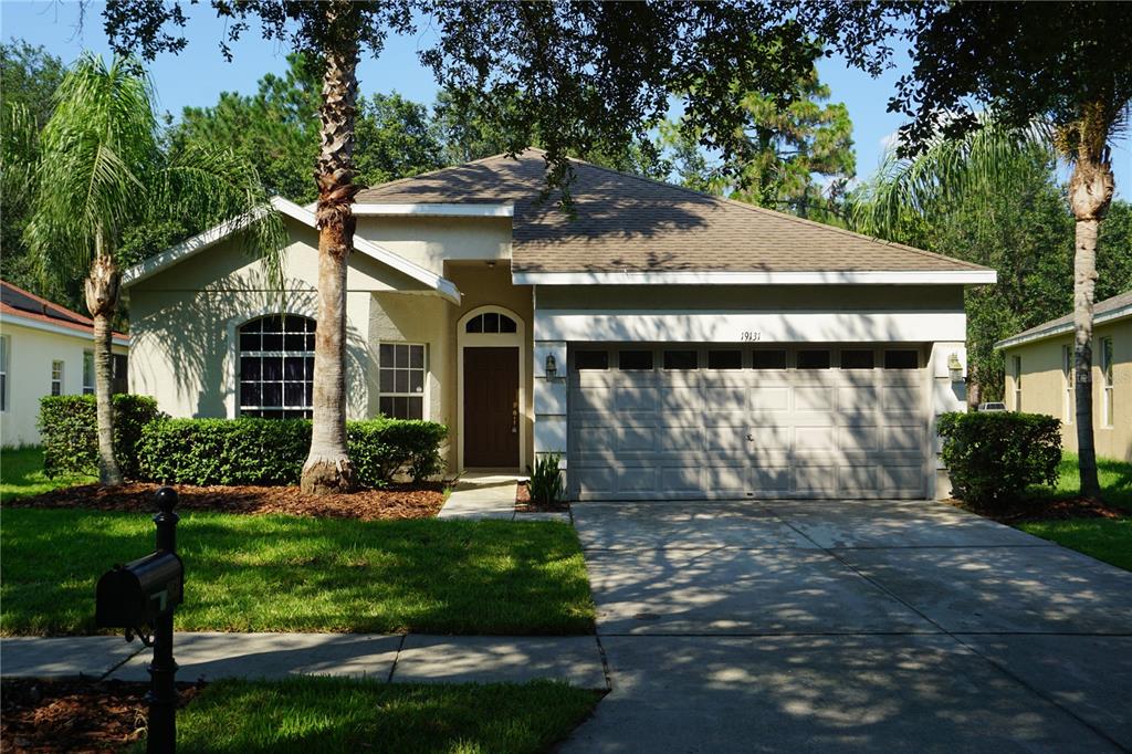 A single-story house with a beige stucco exterior, a two-car garage, and a front lawn — 19131 CYPRESS REACH LANE, TAMPA, FL
