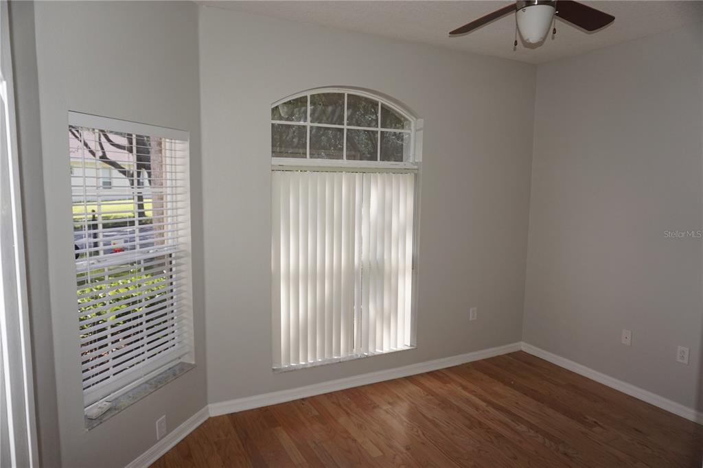 An empty room features hardwood floors, light gray walls, a ceiling fan, and two windows — 19131 CYPRESS REACH LANE, TAMPA, FL
