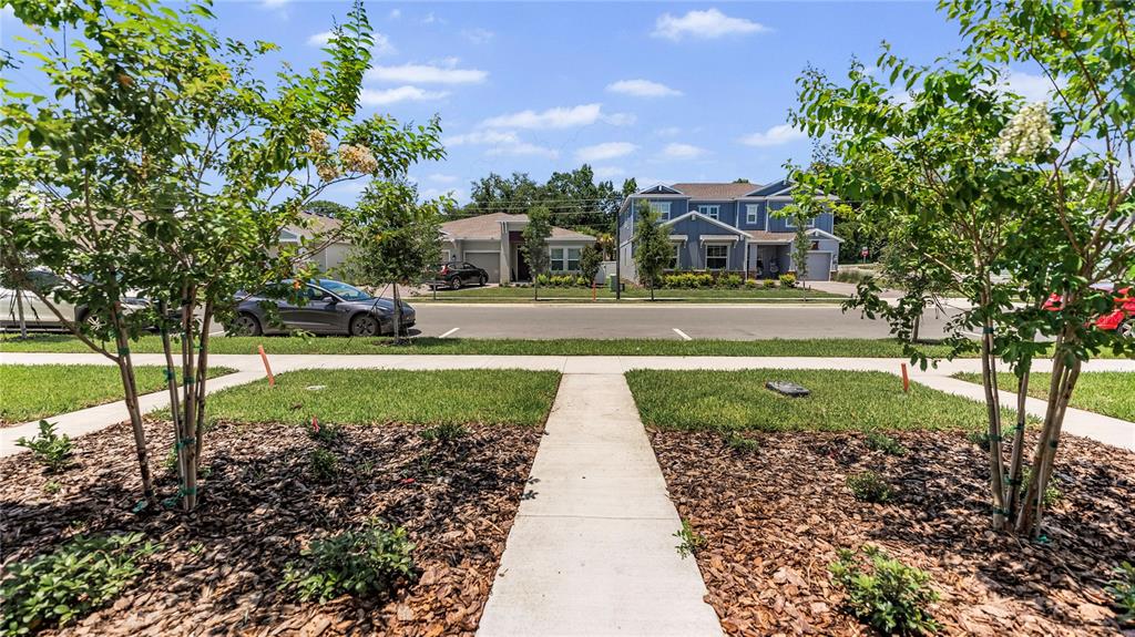 A sidewalk leads toward a street with parked cars and suburban houses under a blue sky — 2136 RIDER RAIN LANE, APOPKA, FL