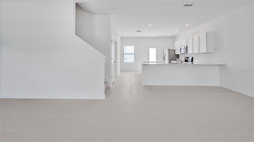 A bright, open-concept kitchen and living area featuring white cabinetry, tile flooring, and stairs — 2136 RIDER RAIN LANE, APOPKA, FL