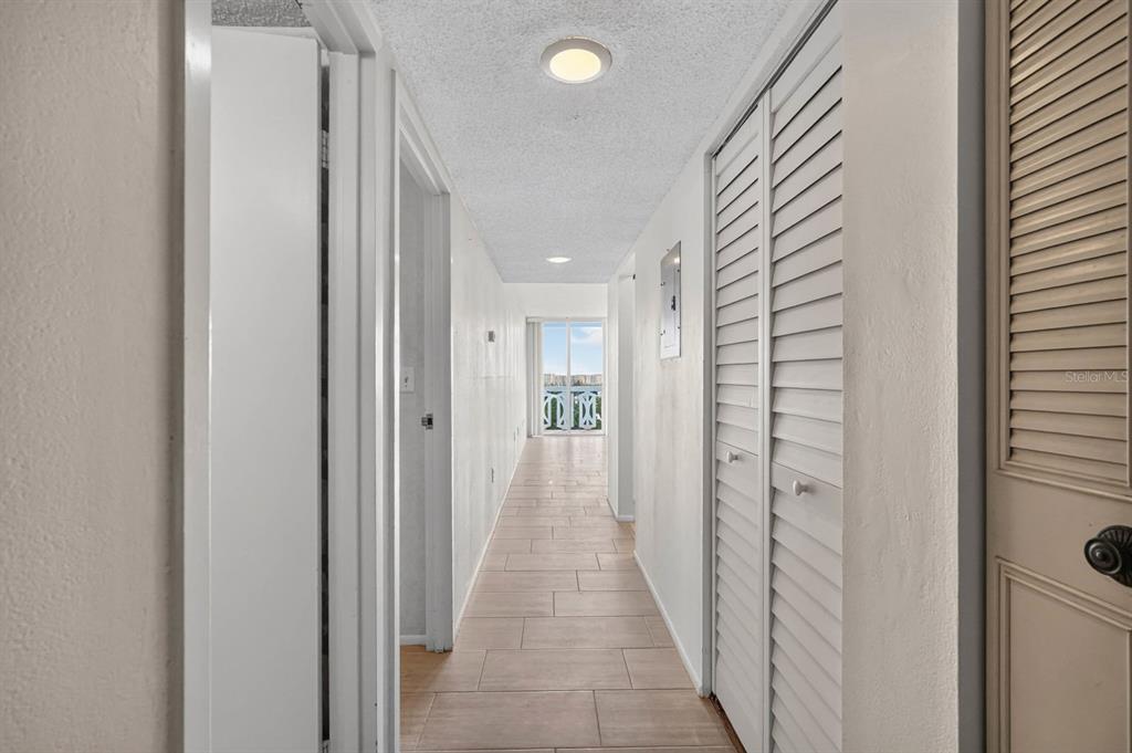 A long hallway with light-colored tile flooring leads toward a bright room with sliding doors — 925 N HALIFAX AVENUE UNIT 710, DAYTONA BEACH, FL