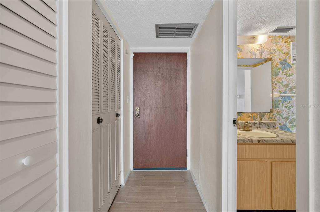 A hallway features a brown wooden door, louvered closet doors, and an adjacent bathroom vanity — 925 N HALIFAX AVENUE UNIT 710, DAYTONA BEACH, FL