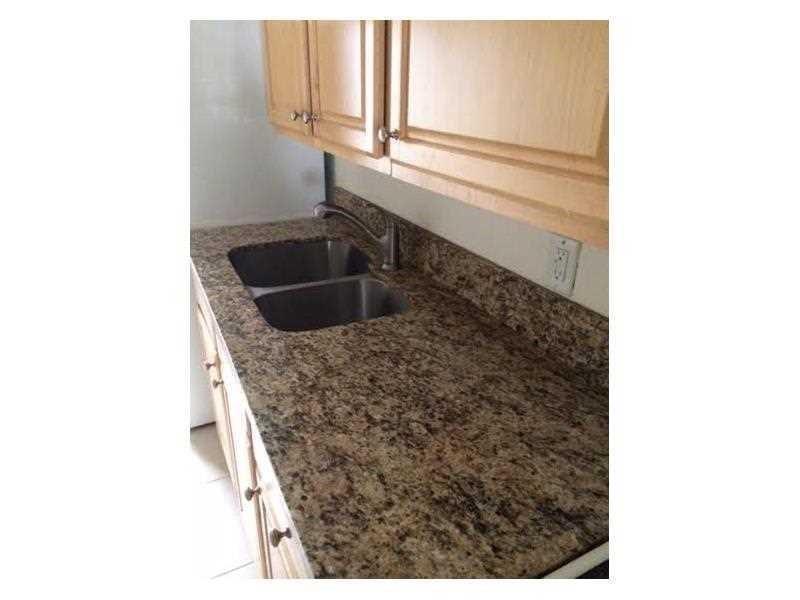 A kitchen features light wood cabinets, a granite countertop, and a stainless steel double sink — LAUDERDALE BY THE SEA, FL