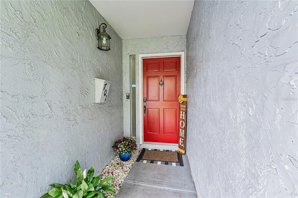 A red front door is set in a gray stucco entryway with a house number — 701 SAINT MICHAEL LANE, ALTAMONTE SPRINGS, FL