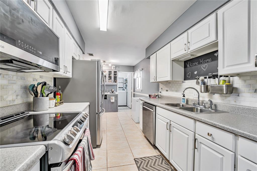 A galley kitchen features white cabinets, stainless steel appliances, and light-colored tile flooring — 701 SAINT MICHAEL LANE, ALTAMONTE SPRINGS, FL