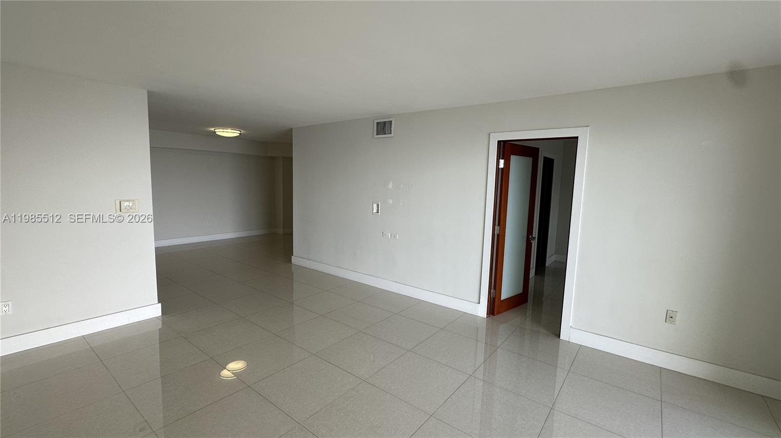 An empty room features light-colored tile flooring, white walls, and a wooden door with glass — 2333 Brickell Ave # 1009, Miami FL 33129, MIAMI, FL