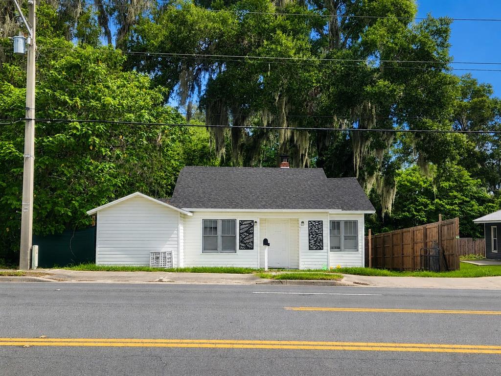 A small, white, single-story house with a dark shingled roof sits beside a paved road — 617 NE 25TH AVENUE, OCALA, FL