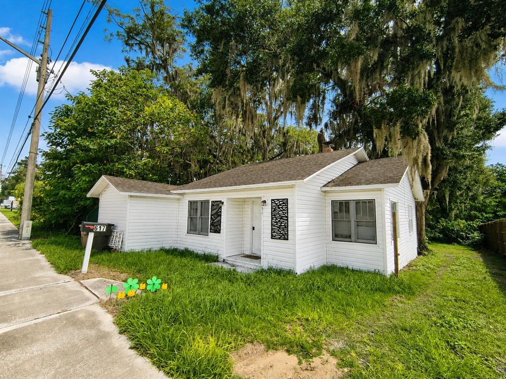 A white, single-story house with a shingled roof stands behind a grassy yard and trees — 617 NE 25TH AVENUE, OCALA, FL
