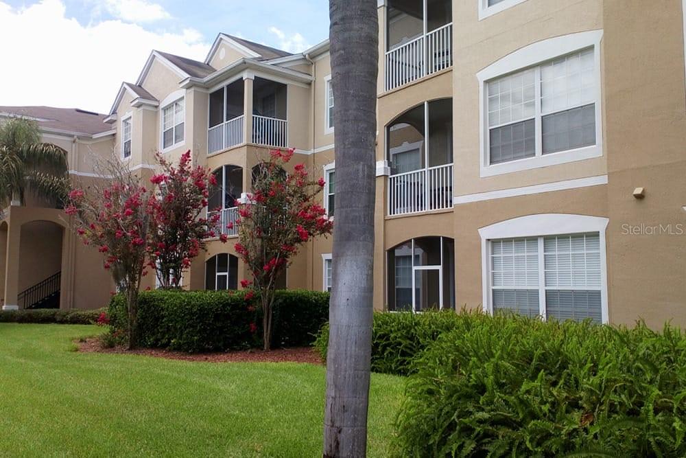 A multi-story apartment building features tan stucco walls, screened balconies, and landscaped grounds — 2307 BUTTERFLY PALM WAY UNIT 102, KISSIMMEE, FL