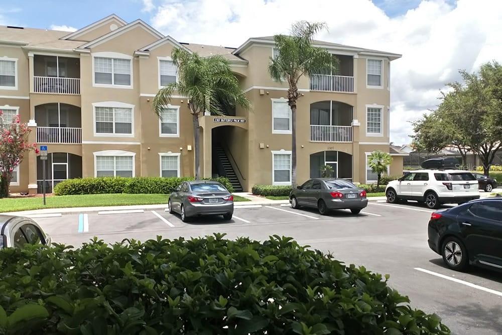 A multi-story apartment building with tan stucco siding and a parking lot in front — 2307 BUTTERFLY PALM WAY UNIT 102, KISSIMMEE, FL