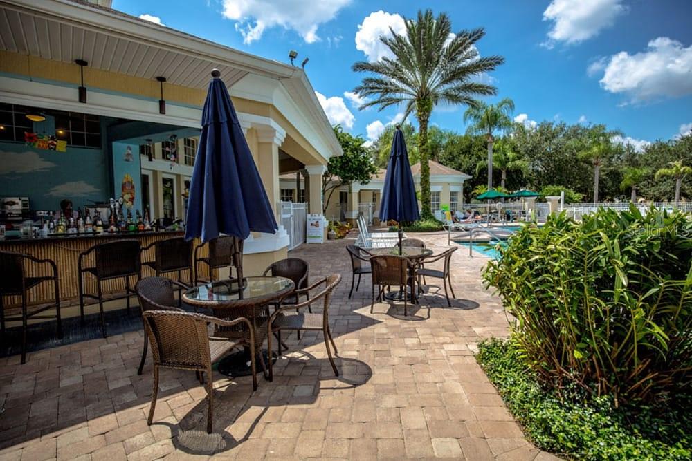 An outdoor patio area features a bar, dining tables with umbrellas, and a swimming pool — 2307 BUTTERFLY PALM WAY UNIT 102, KISSIMMEE, FL