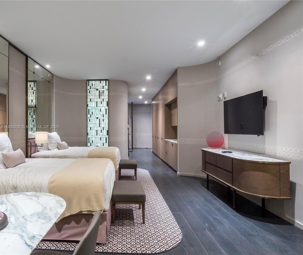 A modern bedroom features two beds, a wall-mounted television, and a curved wooden media console — 801 S Miami Ave # 712, Miami FL 33130, MIAMI, FL