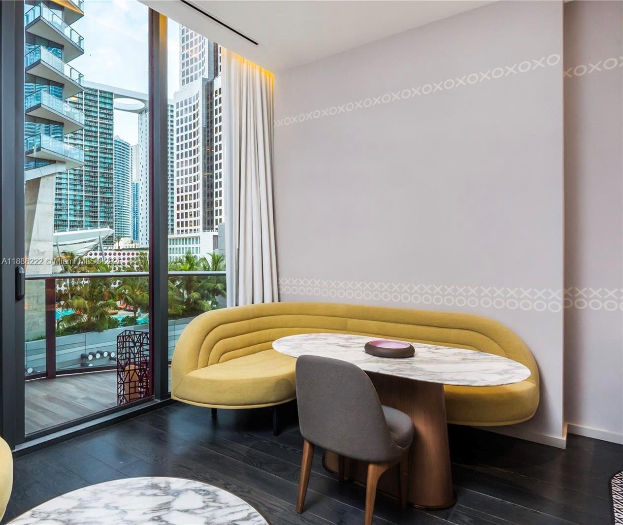 A dining area features a yellow curved banquette, marble table, and floor-to-ceiling city views — 801 S Miami Ave # 712, Miami FL 33130, MIAMI, FL