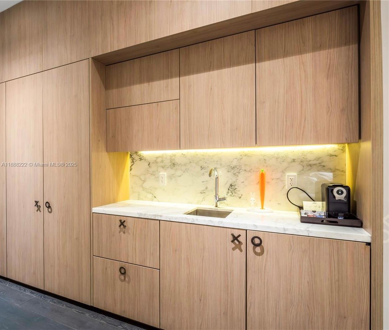 A modern kitchenette features light wood cabinetry, a marble countertop, and a marble backsplash — 801 S Miami Ave # 712, Miami FL 33130, MIAMI, FL