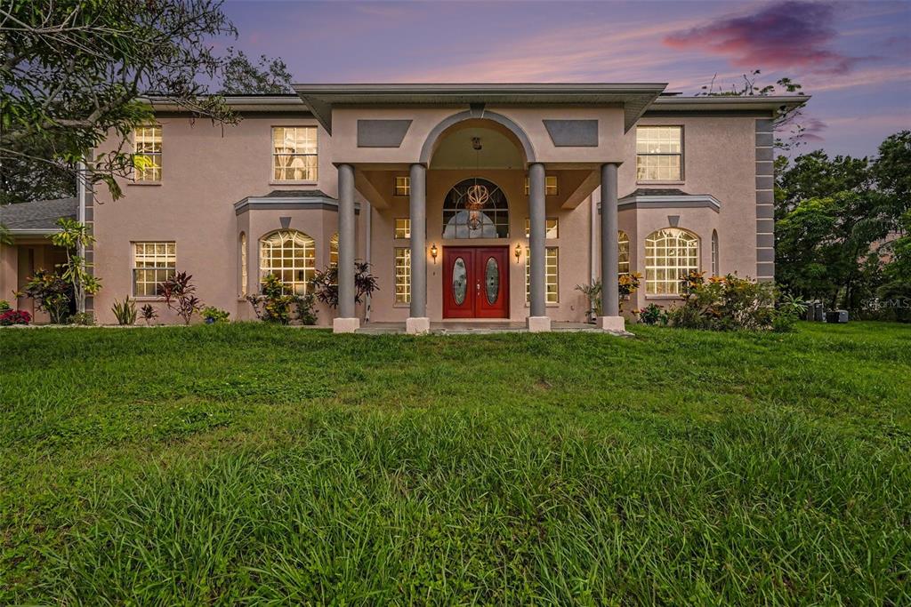 A two-story house with a peach-colored stucco exterior, a grand arched entryway, and red doors — 9723 YESHUA WAY, TAMPA, FL