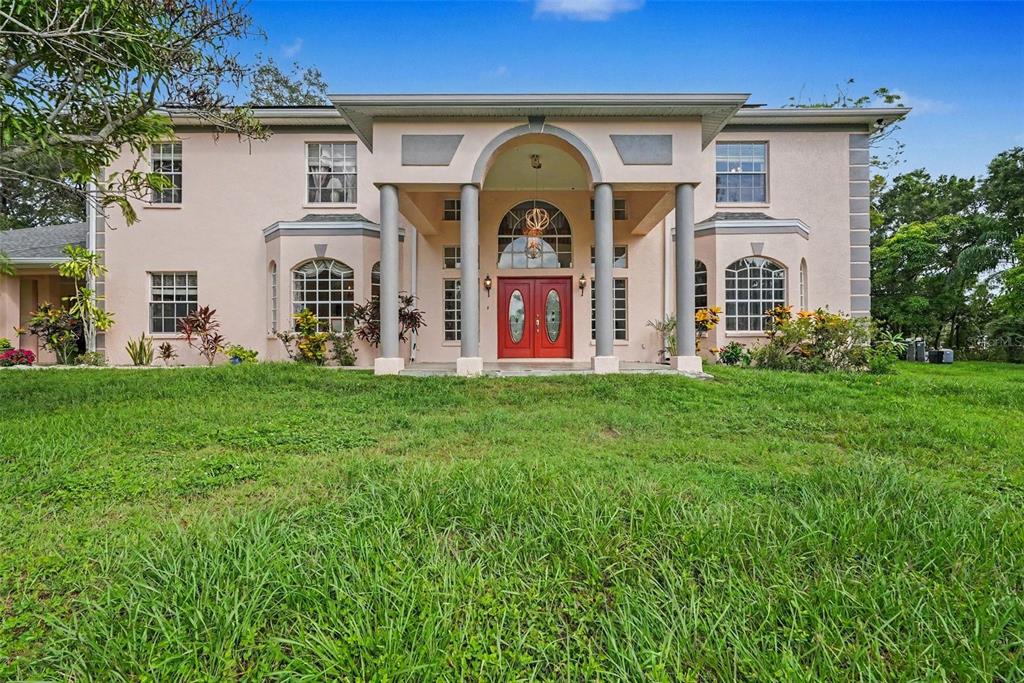A two-story house with a peach-colored stucco exterior, four columns, and red double front doors — 9723 YESHUA WAY, TAMPA, FL