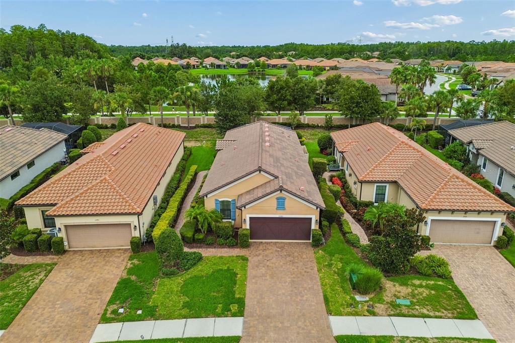 An aerial view shows three suburban houses with terracotta-tiled roofs and paver driveways — 11503 CALLISIA DRIVE, ODESSA, FL