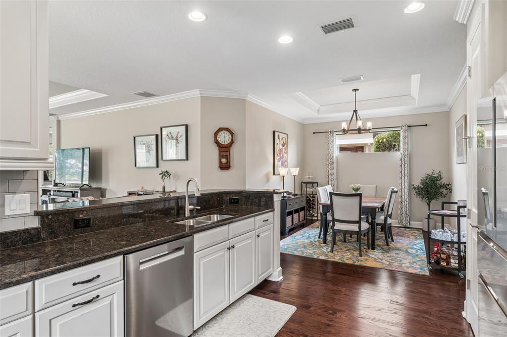 A kitchen with dark granite countertops and white cabinets overlooks a dining area with hardwood floors — 11503 CALLISIA DRIVE, ODESSA, FL