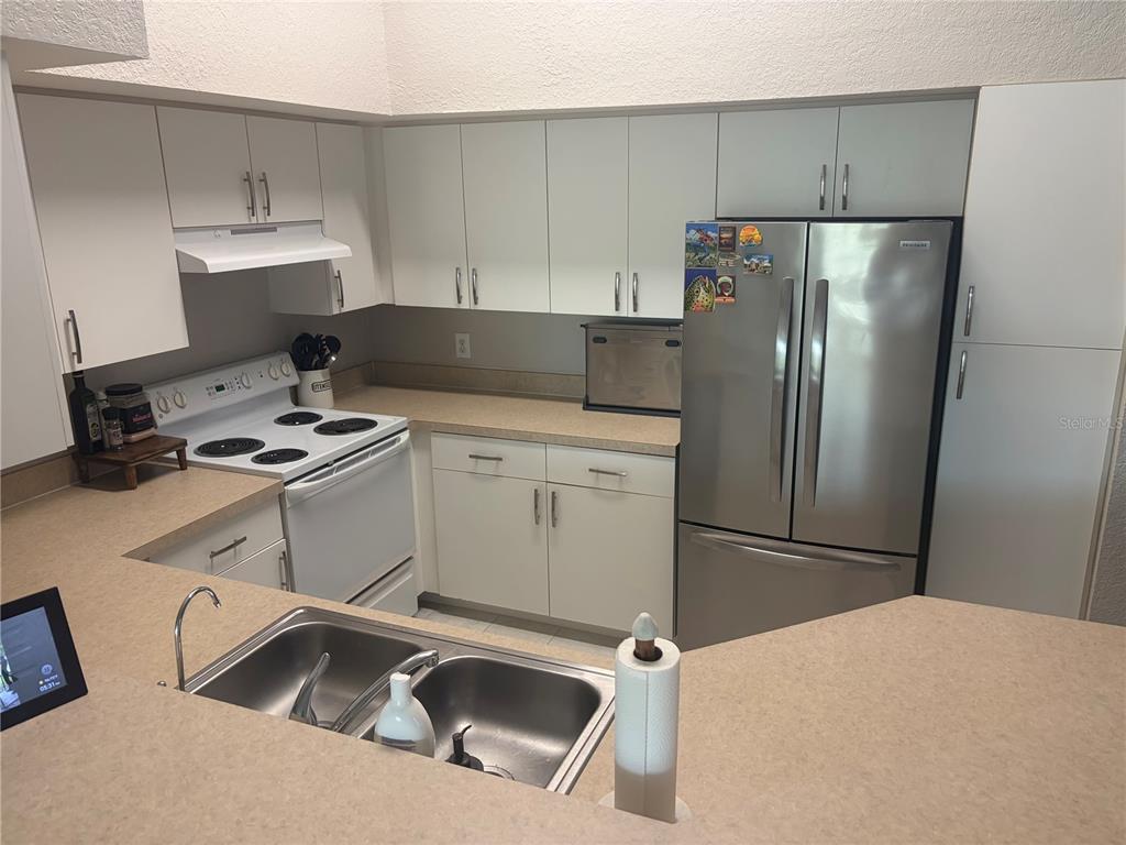A kitchen features white cabinets, a stainless steel refrigerator, a white stove, and beige countertops — 4140 CENTRAL SARASOTA PARKWAY UNIT 1235, SARASOTA, FL