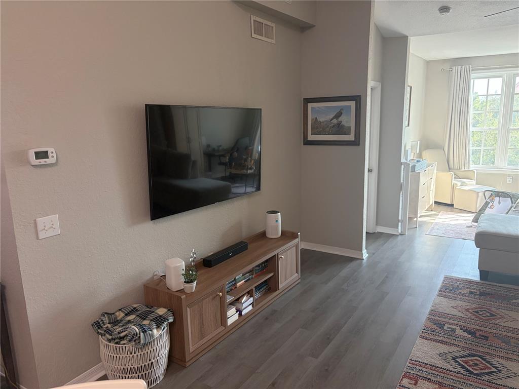 A living room features a wall-mounted television, a wooden media console, and gray flooring — 4140 CENTRAL SARASOTA PARKWAY UNIT 1235, SARASOTA, FL