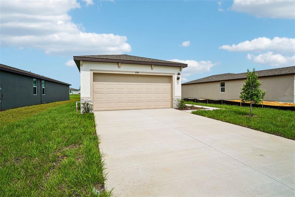 A single-story house exterior features a beige garage door, concrete driveway, and stone accents — 3739 MOSCATO DRIVE, BROOKSVILLE, FL