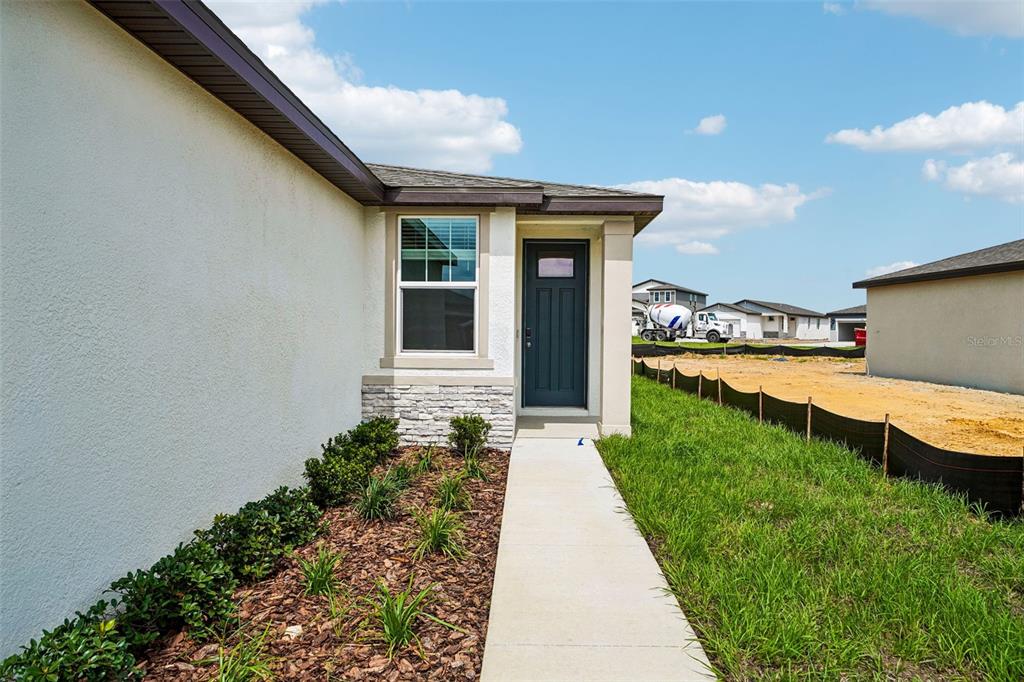A concrete walkway leads to the dark front door of a house with stucco siding — 3739 MOSCATO DRIVE, BROOKSVILLE, FL