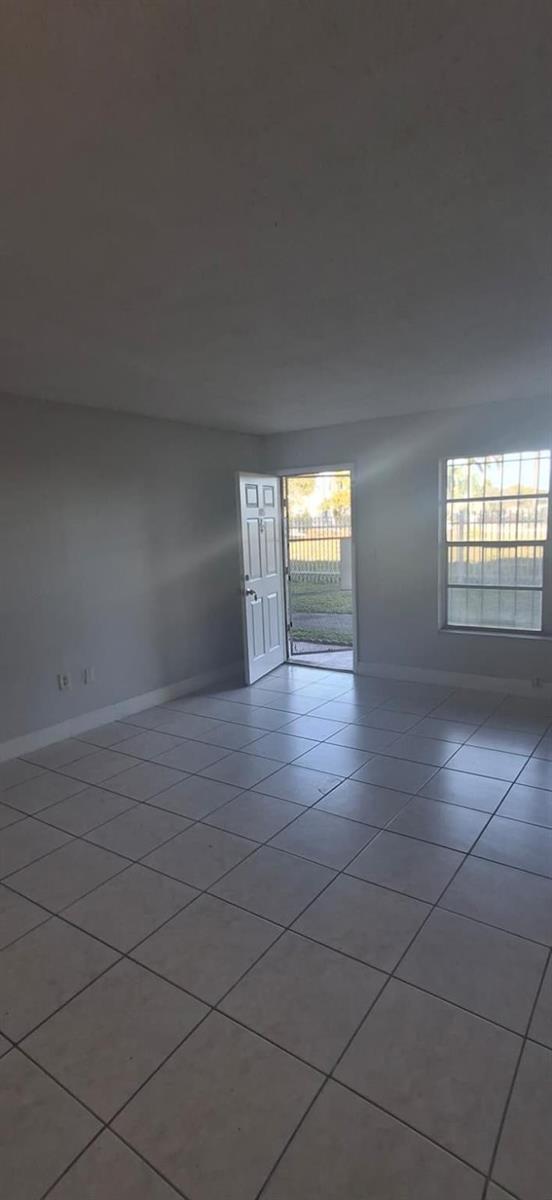 An empty room with light-colored tile flooring, gray walls, a window, and an open door — 251 NW 177th Street # 105, Miami FL 33169, MIAMI, FL