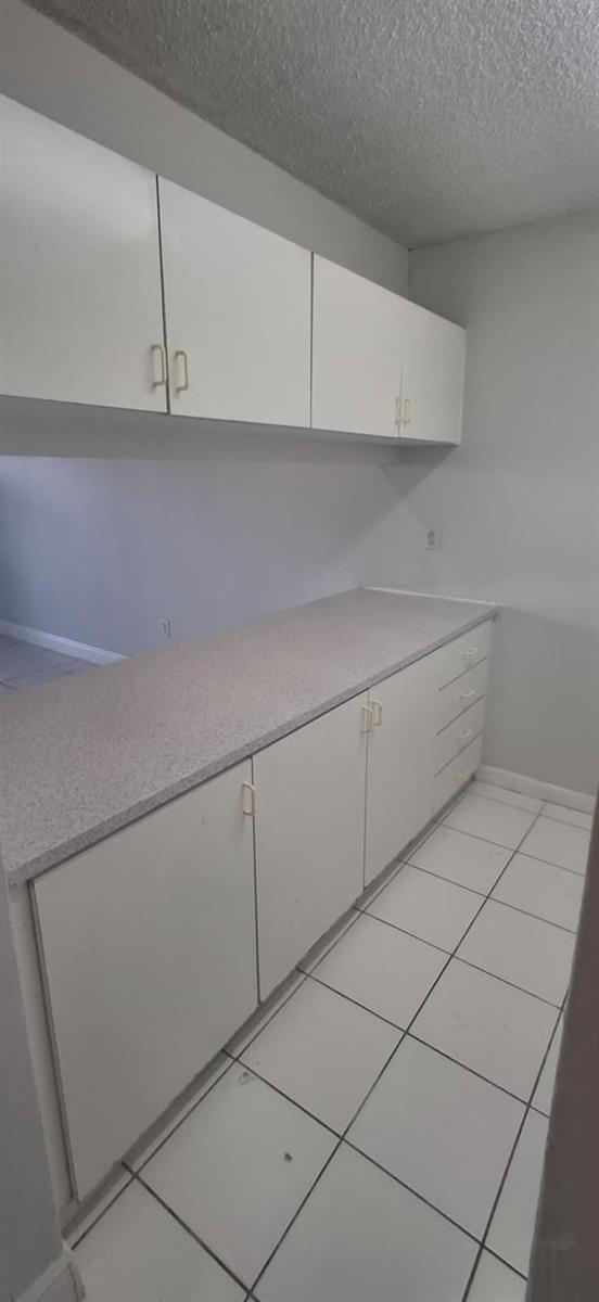 A kitchen features white cabinets, a speckled countertop, and white tile flooring — 251 NW 177th Street # 105, Miami FL 33169, MIAMI, FL
