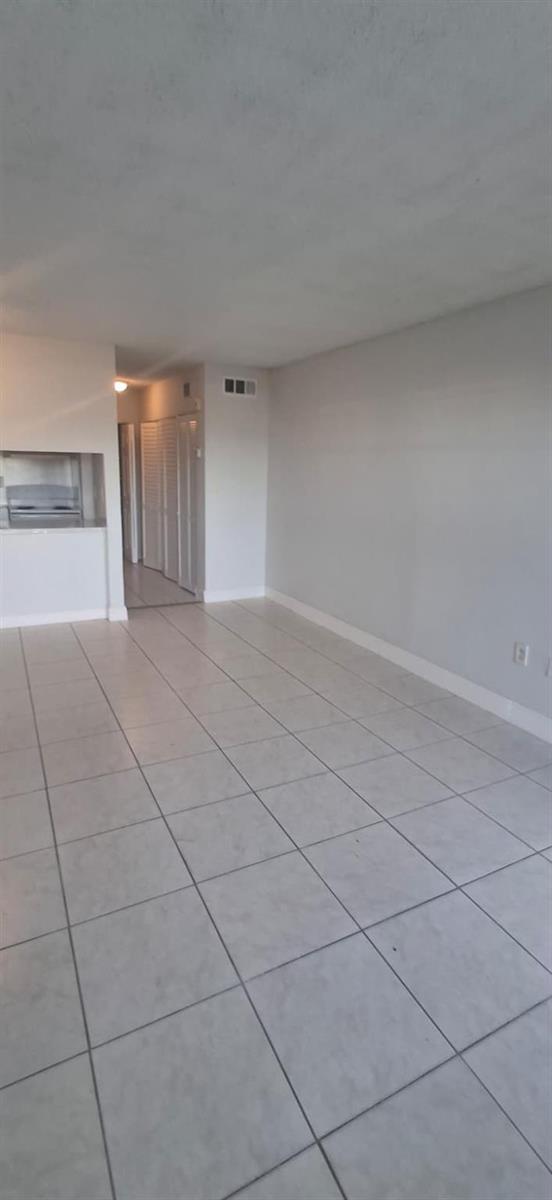 An empty room with light-colored floor tiles and white walls leads to a hallway — 251 NW 177th Street # 105, Miami FL 33169, MIAMI, FL