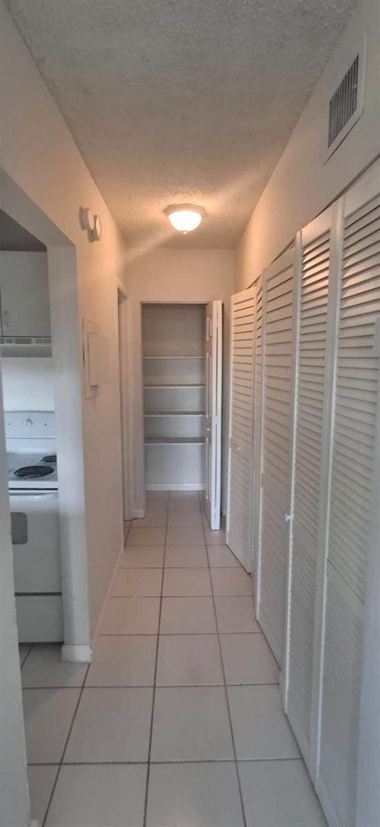 A hallway with white tile flooring leads to a pantry with shelves and louvered closets — 251 NW 177th Street # 105, Miami FL 33169, MIAMI, FL