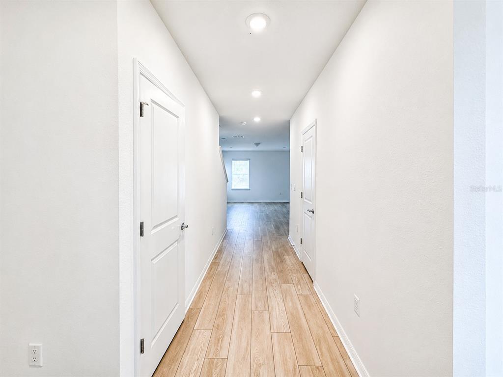 A hallway with white walls, light wood-look flooring, and two closed white doors — 5646 ENCHANTED MEADOW ALY, CLERMONT, FL