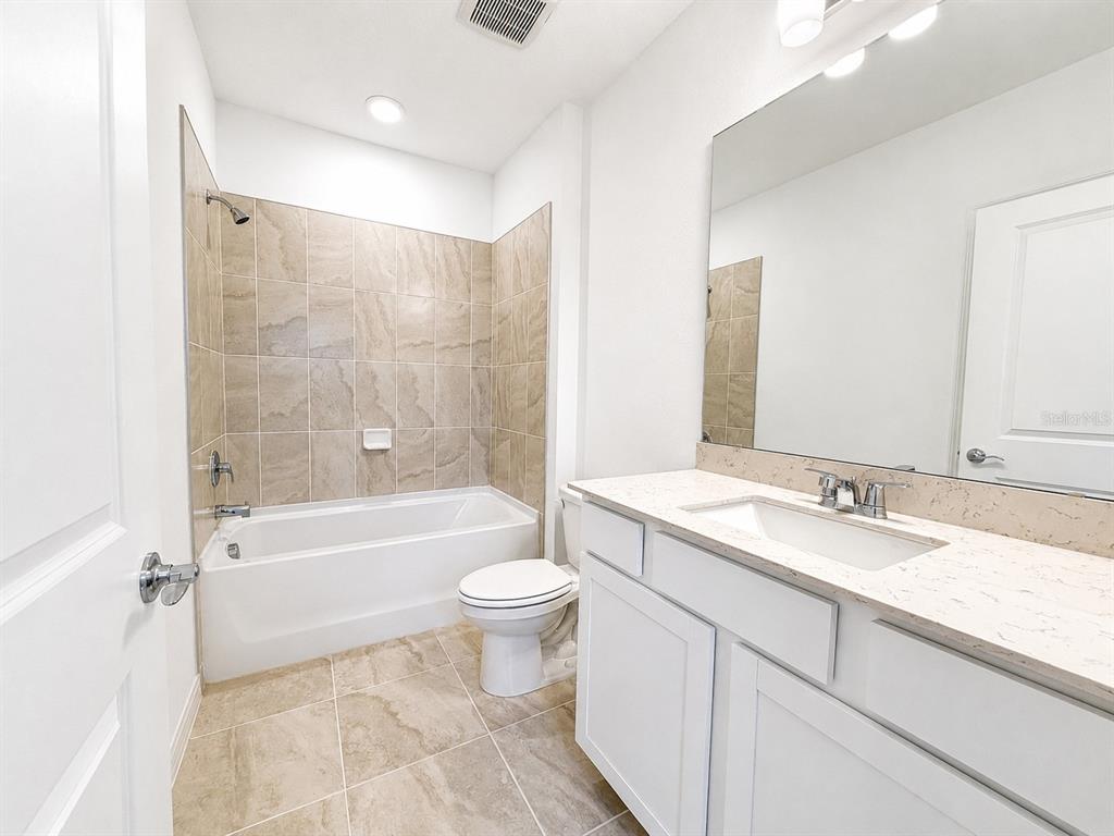 A bathroom features a tiled tub-shower combination, a white vanity, and a toilet — 5646 ENCHANTED MEADOW ALY, CLERMONT, FL