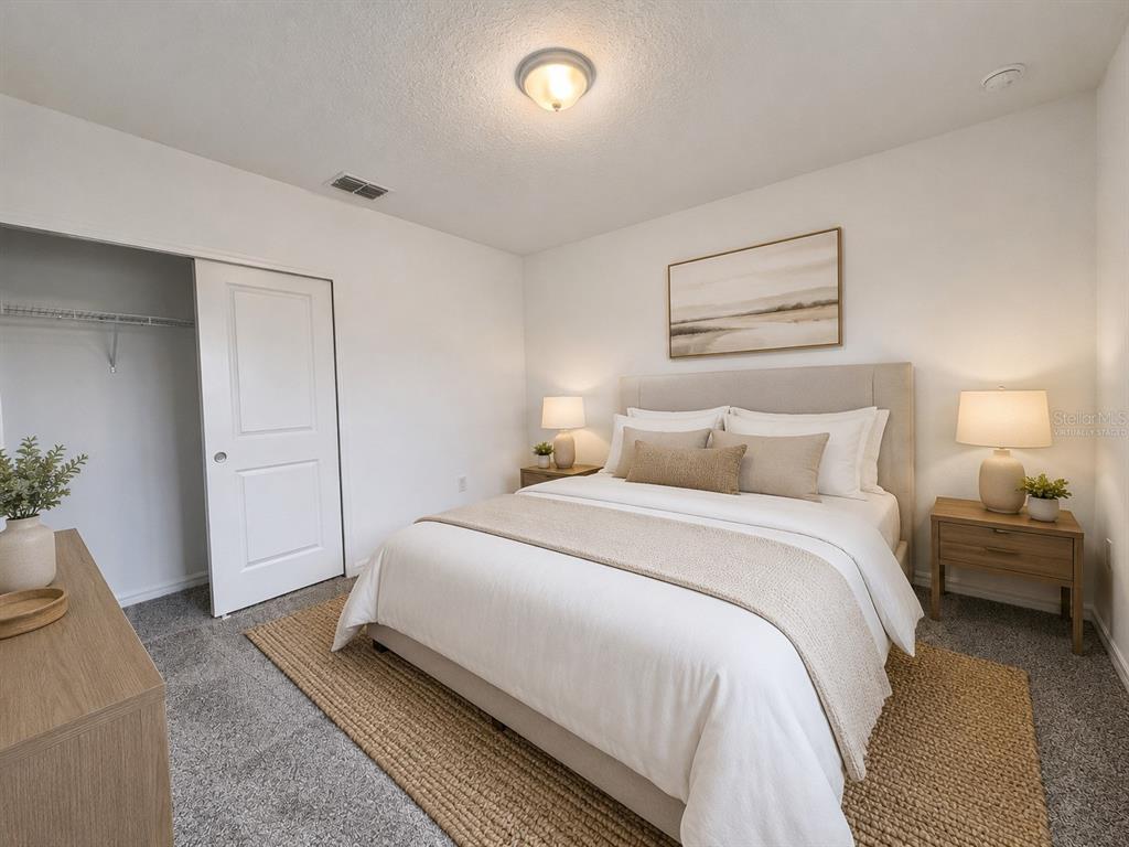 A bedroom features a bed with neutral bedding, two nightstands, and a closet with white doors — 5646 ENCHANTED MEADOW ALY, CLERMONT, FL