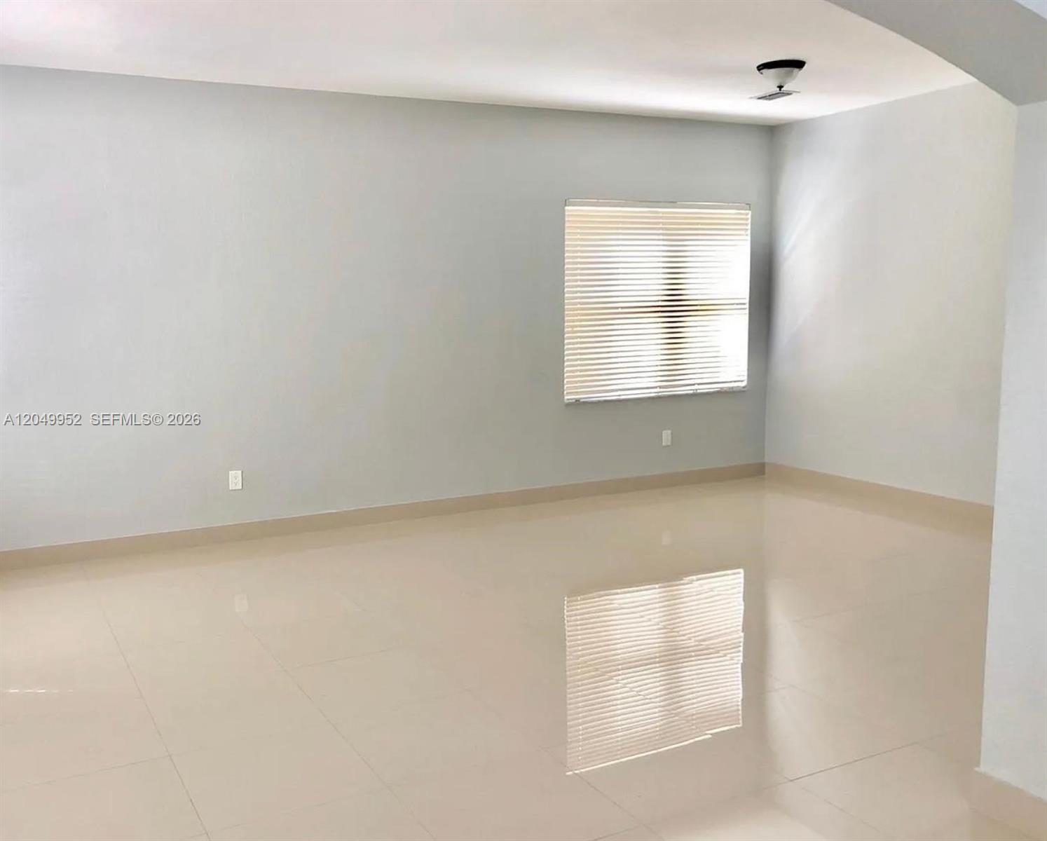 An empty room features light-colored walls, large glossy floor tiles, and a window with blinds — 3965 NE 15th St, Homestead FL 33033, HOMESTEAD, FL