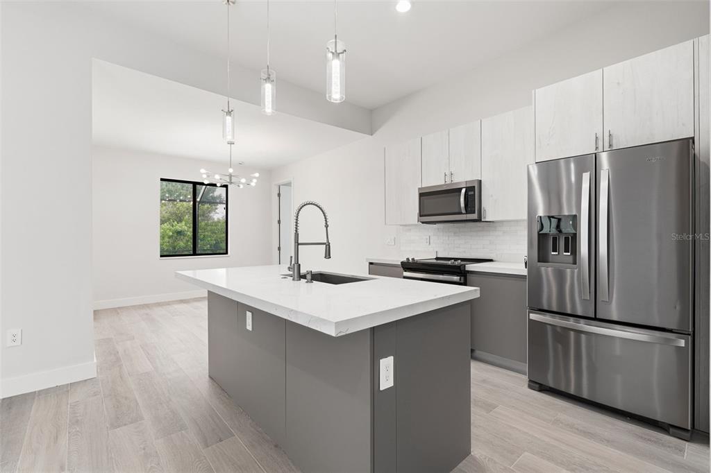 A modern kitchen features a gray island, white upper cabinets, and stainless steel appliances — 14319 ALLENSWORTH AVENUE, PORT CHARLOTTE, FL