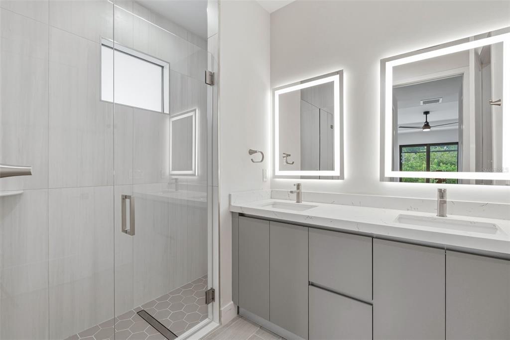 A modern bathroom features a glass-enclosed shower, dual vanity with gray cabinets, and backlit mirrors — 14319 ALLENSWORTH AVENUE, PORT CHARLOTTE, FL
