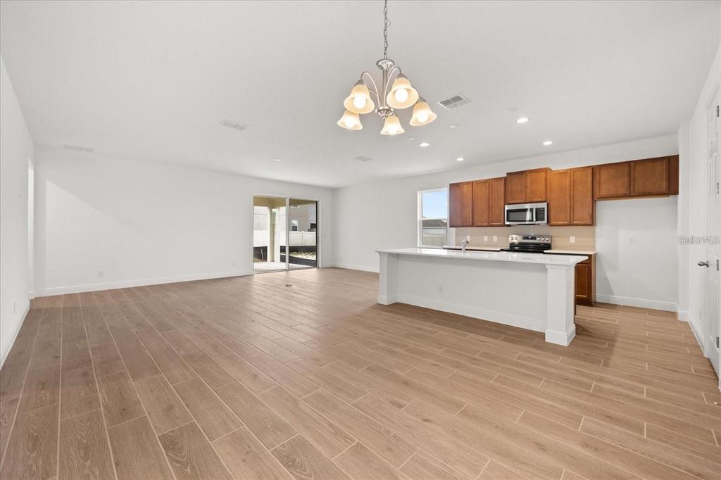 An open-concept kitchen and living area features wood-look tile flooring and a central island — 7731 SCICLI WAY, CLERMONT, FL