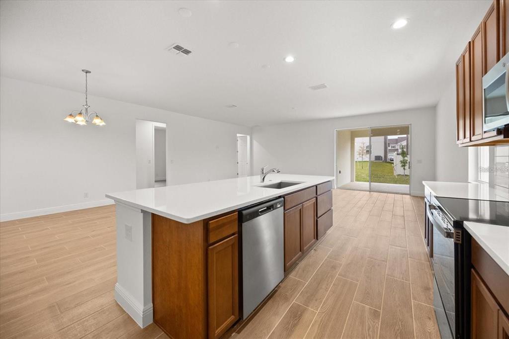 A kitchen with wood cabinets, a white island, and tile flooring opens to a patio — 7731 SCICLI WAY, CLERMONT, FL