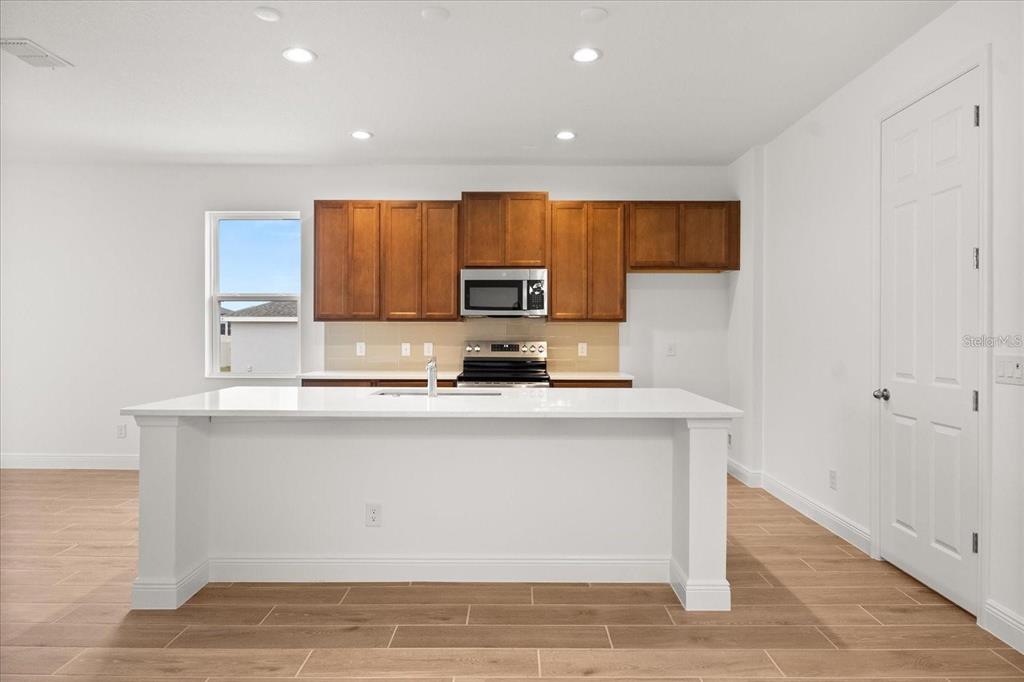 A kitchen features a white island, wooden cabinets, stainless steel appliances, and light wood flooring — 7731 SCICLI WAY, CLERMONT, FL