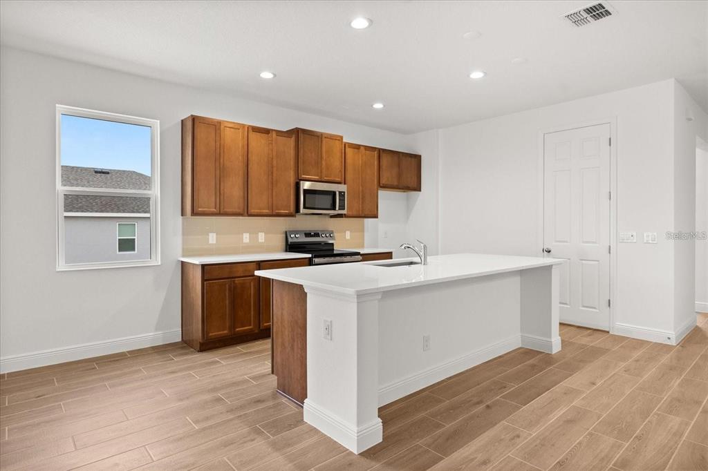 A kitchen features wood cabinets, white countertops, a center island, and light-colored wood-look flooring — 7731 SCICLI WAY, CLERMONT, FL