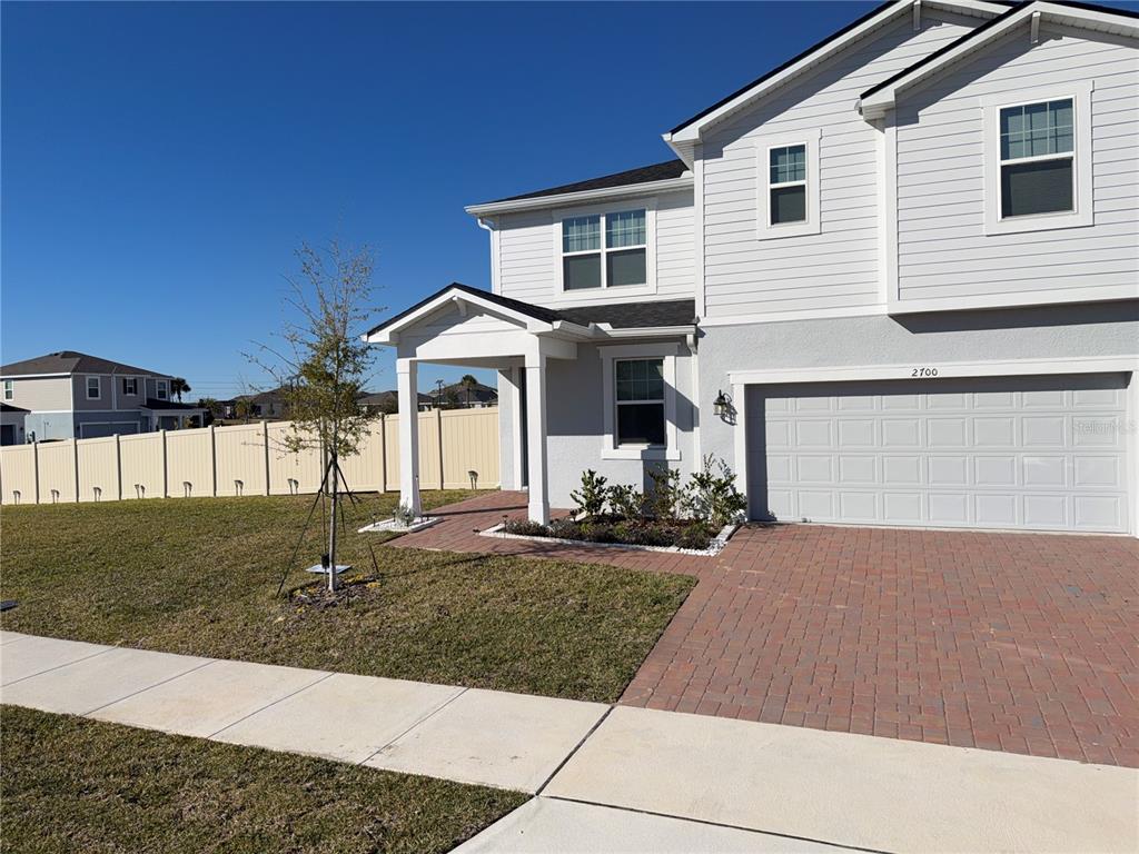 A two-story house features light gray siding, a brick driveway, and a covered front entryway — 2700 SWEET ACACIA DRIVE, CLERMONT, FL