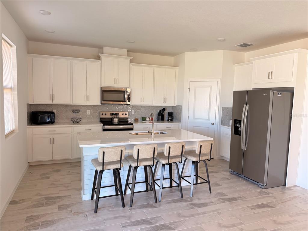 A modern kitchen features white cabinetry, a central island with four stools, and stainless appliances — 2700 SWEET ACACIA DRIVE, CLERMONT, FL